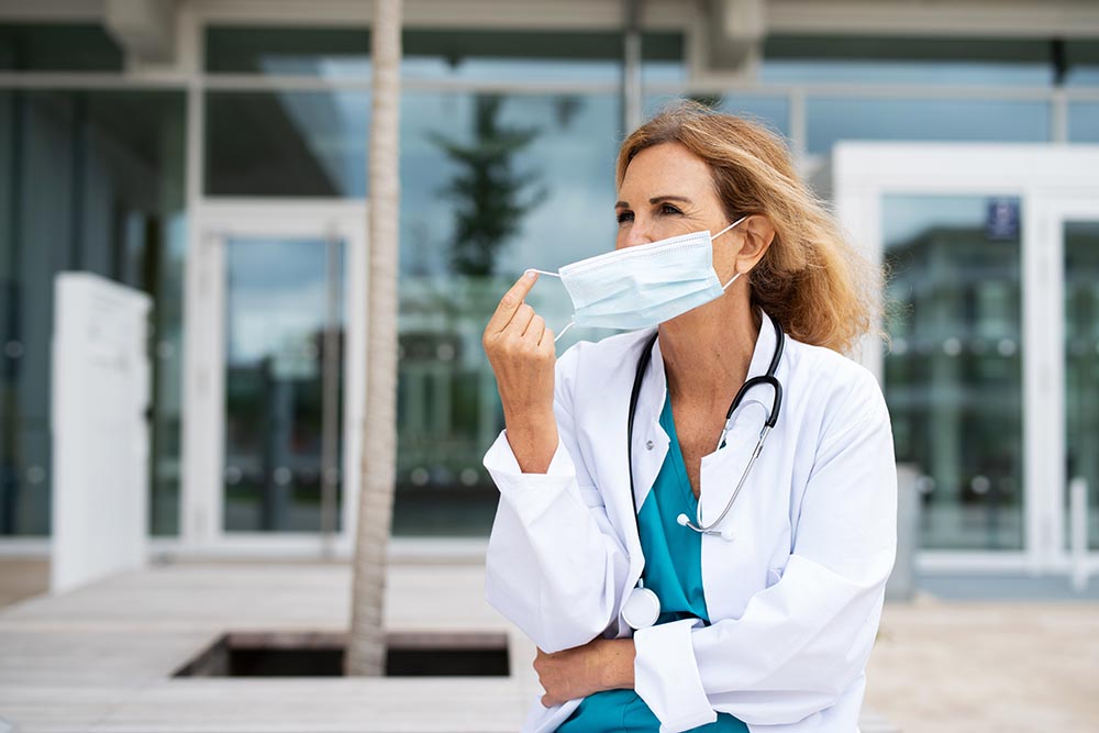 A physician outside a hospital taking off her mask